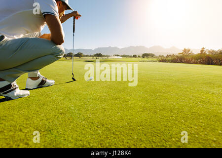 Pro golf player aiming shot with club on course. Male golfer on putting green about to take the shot. Stock Photo