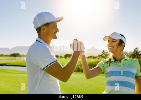 Shot of male and female friends giving high-five at golf course. Professional golfers shaking hands after the game. Stock Photo