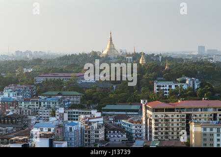 View of Yangon, Myanmar, from above in daylight and golden Shwedagon Pagoda on a lush hill. Stock Photo