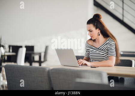 Young female entrepreneur reading electronic book on laptop during lunch in modern restaurant interior. Elegant businesswoman chatting on tablet while sitting in comfortable coffee shop. Stock Photo