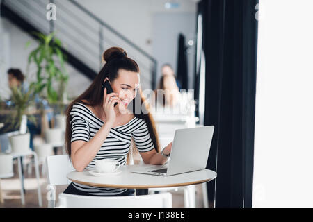 Portrait of executive financial woman sitting at desk and working on laptop while making call. Stock Photo