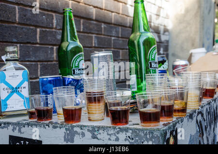 Empty beer bottles and plastic shot glasses left abandoned on a ledge outside in the street. Stock Photo