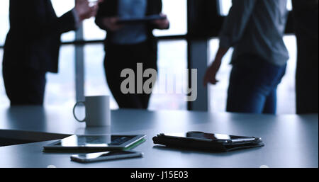 Devices on table with business people in background in modern office building Stock Photo