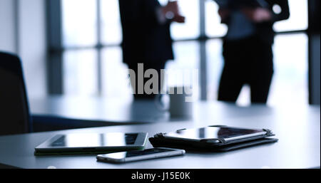 Devices on table with business people in background in modern office building Stock Photo