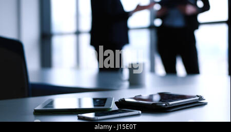 Devices on table with business people in background in modern office building Stock Photo