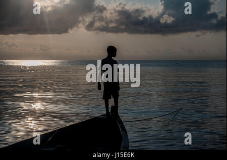 A young boy stands on the bow of a moored boat in Lake Malawi Stock Photo