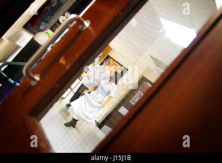 NHS medical UK hospital View through window through to ward reception with medical staff walking in background Stock Photo