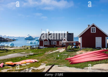 Sea kayaks upside down on ground by coast with icebergs from floating offshore in Disko Bay in summer. Ilulissat (Jakobshavn) Greenland Stock Photo