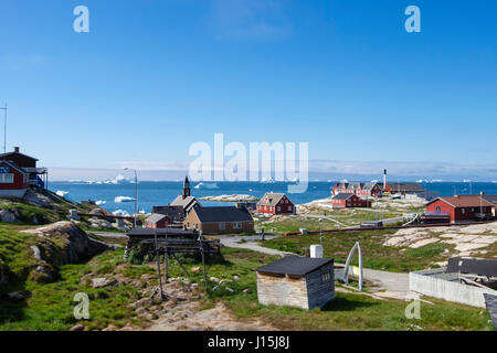 Wooden buildings and view to icebergs floating in sea in Disko Bay off the west coast in summer. Ilulissat (Jakobshavn), Qaasuitsup, Greenland Stock Photo