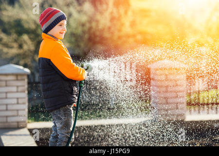 Little boy watering flowers with sunset background Stock Photo