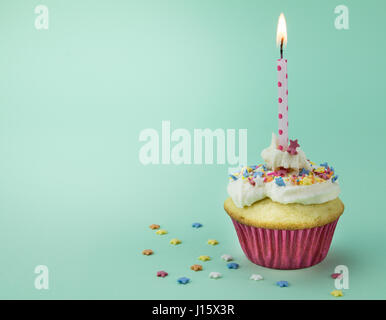 One cupcake with lit candle and star sprinkles isolated on green background Stock Photo