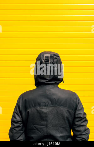 Facing problems and challenging obstacles in life, woman in hooded winter jacket in front of the wall Stock Photo