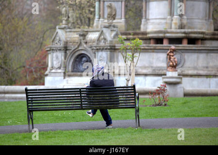 Asian African refugee dressed Hijab scarf  in the UK everyday scene sitting near cherub in park Stock Photo