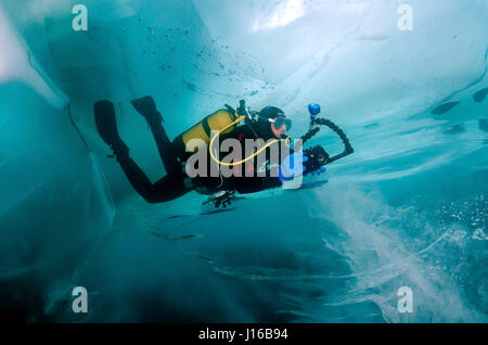 SIBERIA: A diver is ice-cubed inside the passage of ice, Lake Baikal.  AN ICE-CUBED diver took an extraordinary journey INTO an underwater  lump of ice. Pictures taken from the world’s largest lake, Russia’s freezing Lake Baikal, show an adventurous group of ice-divers as they penetrate the ice and jump in for an hour-long dip of a lifetime. Captured at up 50-feet deep under the crust of ice, photographer Andrey Nekrasov, 42, descended from the frozen surface on a quest to record images from the 2,500-foot-deep lake – which has five-times the volume of all five Great Lakes of North America. An Stock Photo