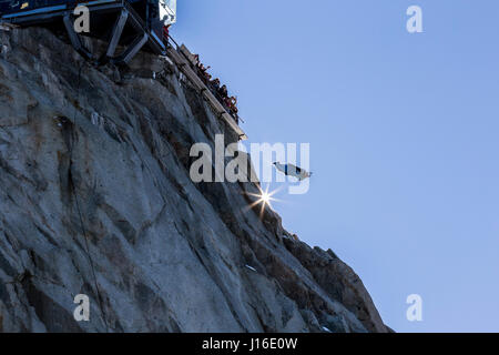 Wingsuit jumper jumping off mountain peak under cheering crowd Stock Photo