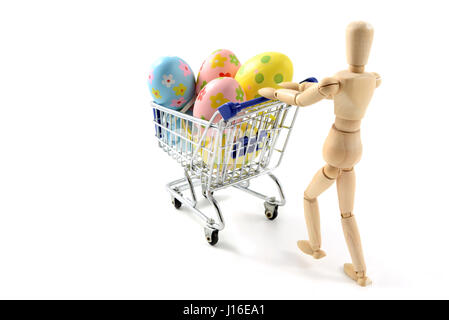 wooden mannequin shopping easter eggs in shopping cart on white isolated background. Stock Photo