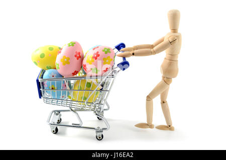 wooden mannequin shopping easter eggs in shopping cart on white isolated background. Stock Photo