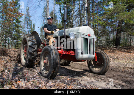 Man driving a vintage tractor on a dirt road in the woods. Stock Photo