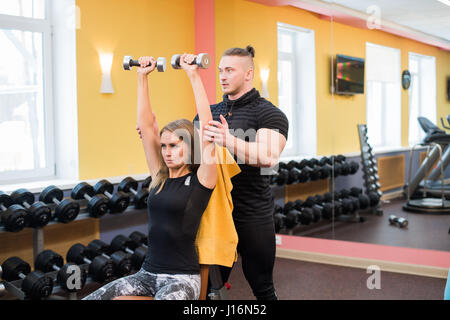 Woman with her personal fitness trainer in the gym exercising power gymnastics with a barbell Stock Photo