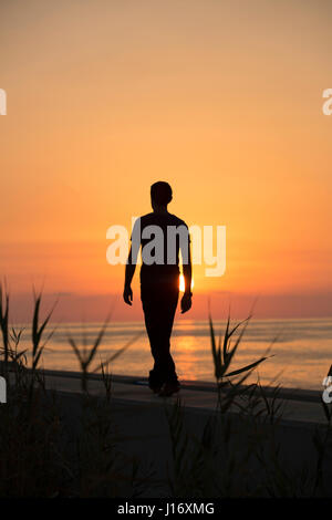 Full length silhouette of a male figure walking on the beach at sunset