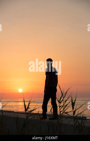 Full length silhouette of a male figure walking on the beach at sunset