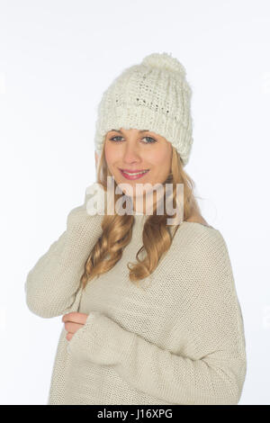 Happy beautiful blond woman wearing a wool hat and jumper smiling against a white background Stock Photo