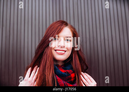 Close up view of attractive happy Caucasian woman with ginger hair wearing stylish clothes looking and smiling at the camera posing against wall. Youth and happiness concept Stock Photo
