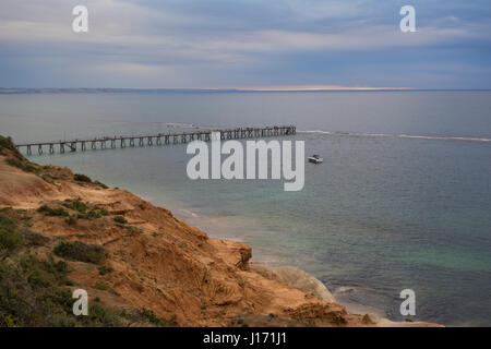 A pastel sunset seen from the cliffs, looking out over the Port Noarlunga jetty and an anchored fishing speed boat. Situated in the outer coastal subu Stock Photo