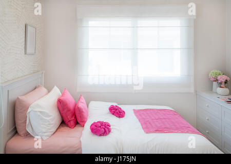 Interior of White bedroom with double bed and pink pillows and bookshelf at home. Stock Photo