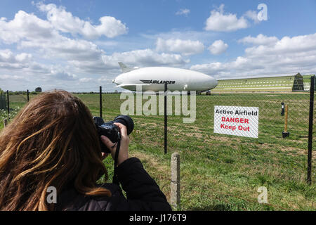 Cardington, Bedfordshire, UK. 18th Apr, 2017. The Hybrid Air Vehicles Airlander 10 is moored to the new Mobile Mooring Mast (MMM), a female photographer shoots through the mesh fence at the airfield. An Auxiliary Landing System (ALS) has been added which allows the aircraft to land safely at a greater range of landing angles. Photo Credit: Mick Flynn/Alamy Live News Stock Photo