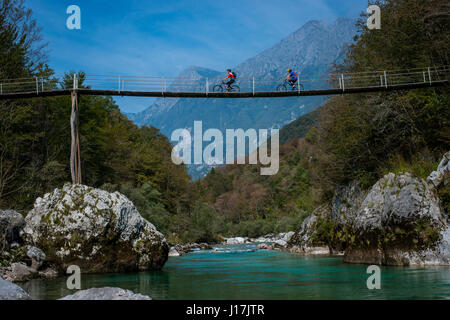 Mountain bikers ride a wooden bridge over the Soca river in Slovenia, Europe. Stock Photo