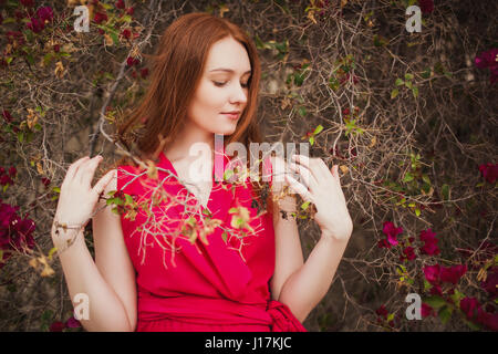 Beautiful redhead girl in the red dress in the Bush. Stock Photo