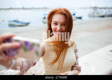The red-haired girl photographed themselves on the phone on the background of the boats. Selfie Stock Photo
