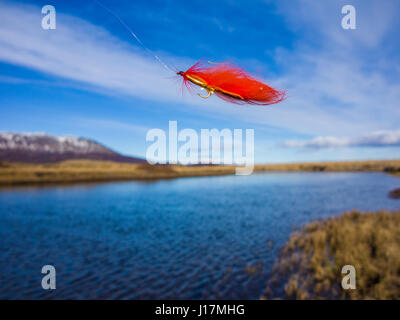 An orange fishing f;lie flutters in the wind before being cast Stock Photo