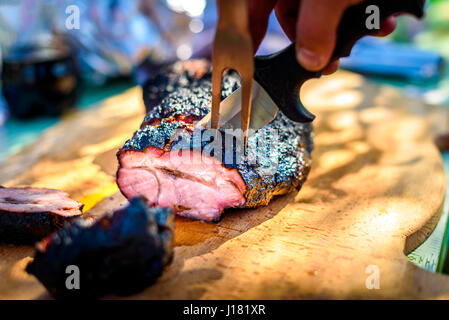 Cutting delicious roast beef pork meat from slow cooking smoker. Serving and cutting piece of juicy tender honey and sauce glazed piece of meat on a w Stock Photo
