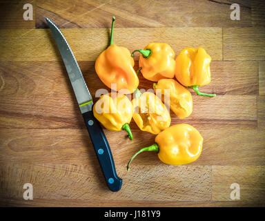 Yellow orange ripe habanero hot chili peppers on a wooden plate from caribbean or mexico. On a wooden cutting desk with a knife Stock Photo