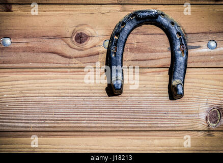 Rusty old vintage weathered horseshoe on wooden background. Horse shoe is hanging on wooden doors as a lucky charm for catching luck. Scene from a far Stock Photo