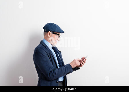 Smart senior man in suit, eyeglasses and cap, holding smartphone Stock Photo