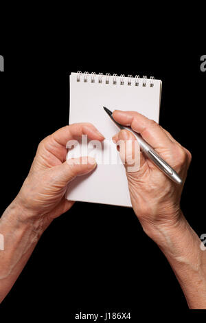 Senior woman hands with pen and blank notebook. Old person writing, calculating or making notes  theme. Isolated on black, clipping path included. Stock Photo