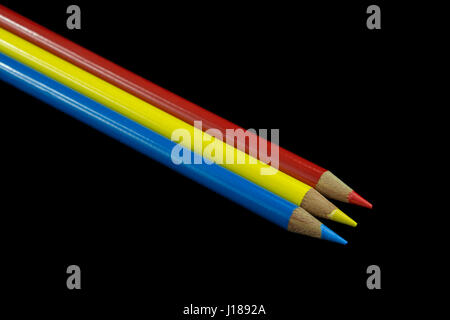 Three primary coloured pencils lined up with a dark black background. Stock Photo