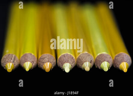 Seven yellow pencils of various hues and shades with a dark black background. Selectively focused only on the pencil points. Stock Photo