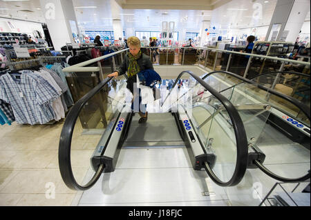 ENSCHEDE, THE NETHERLANDS - APRIL 13, 2017: A woman on the moving staircase in clothes store C&A after it has been reopened. Stock Photo