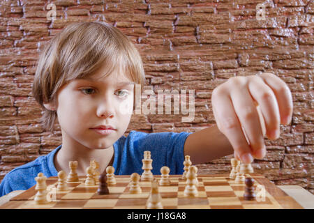 Portrait of a little caucasian boy playing chess and making next move Stock Photo