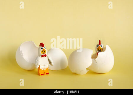 Two lego chickens hatching from eggs on yellow background Stock Photo