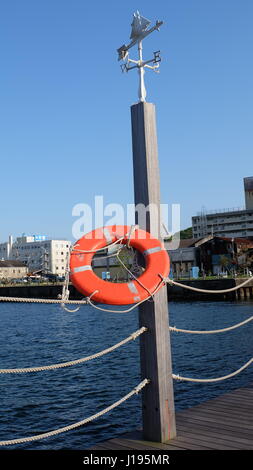 A lifebuoy, also known as ring buoy, lifering, lifesaver, life donut, life preserver or lifebelt, hanging on a pole near the seaside Stock Photo