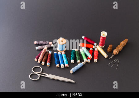Different rolls with red, blue and green polyester and silk thread, needles, scissors and a wooden needle container with grey background Stock Photo