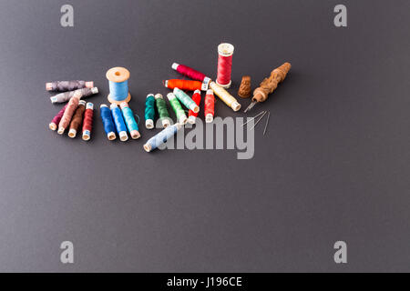 Different rolls with red, blue and green polyester and silk thread, needles and a wooden needle container with grey background Stock Photo