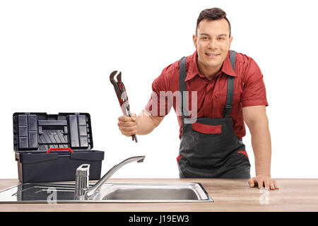 Plumber with a pipe wrench and a toolbox standing behind a sink and looking at the camera isolated on white background Stock Photo