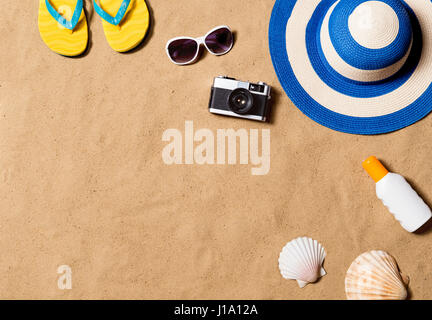 Summer vacation composition with pair of yellow flip flop sandals, hat, sunglasses, sun cream and other stuff on a beach. Sand background, studio shot Stock Photo