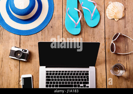 Summer vacation composition with laptop, camera, smart phone, blue flip flop sandals, hat and other stuff on wooden background, studio shot, flat lay. Stock Photo